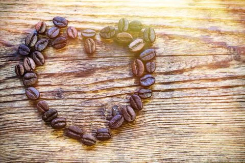 Coffee grains are lined in the shape of a heart on a wooden board. Stock Photos