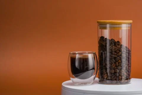 Coffee grains in transparent container and coffee cup on white table. Stock Photos