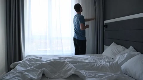 Coffee in hand, the man pulls back the curtains and looks out the window. Stock Footage 307666660