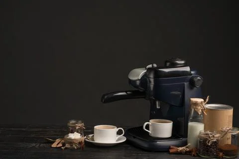 Coffee machine with a cup of coffee, with jars of coffee and milk on a dark b Stock Photos
