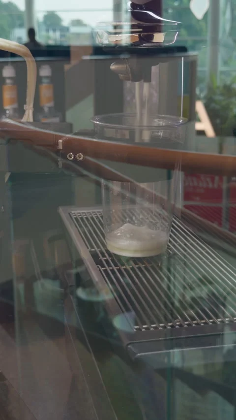 Coffee machine dispensing fresh milk into clear cup inside modern cafe through Stock Footage 345611818
