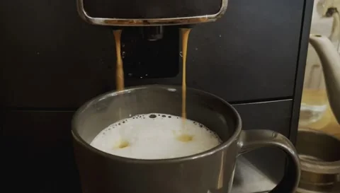 The coffee machine pours cappuccino coffee into a black ceramic cup Stock Footage 217437599