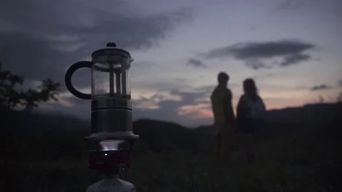 Coffee maker on camping gas stove while couple in background 스톡 동영상 72503530