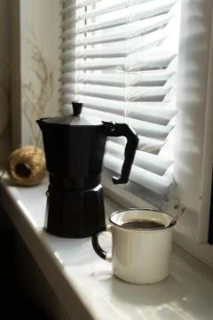 Coffee maker with a cup of freshly brewed coffee on a windowsill Stock Photos