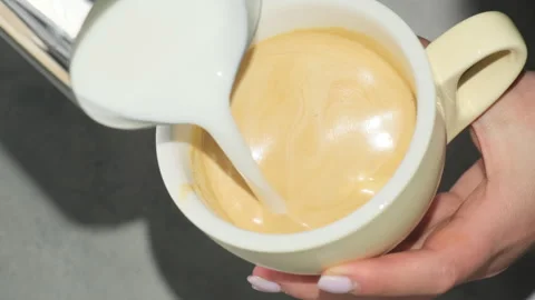 Coffee maker shakes cup of coffee adding milk from mug Video stock 306213625