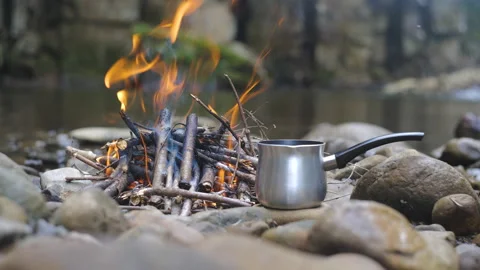 Coffee maker on a stone near a fire on the bank of a stream Stock Footage 208469600