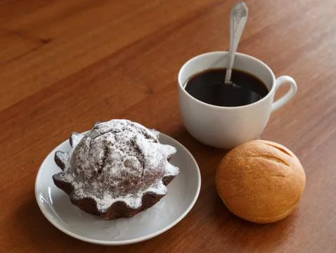 Coffee mug, bun and chocolate cupcake on a small plate. On brown wooden backg Stock Photos