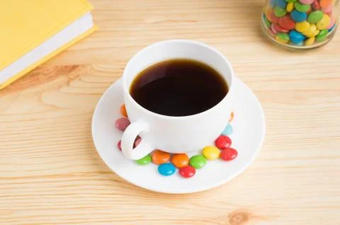 Coffee mug, colored candy in a jar and a yellow diary on a wooden background. Stock Photos