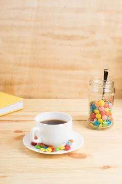 Coffee mug, colored candy in a jar and a yellow diary on a wooden background. Stock Photos