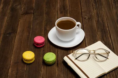 Coffee mug, macarons, notebook and glasses on a wooden table. Side view Stock-Fotos