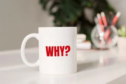 Coffee mug with text - WHY? in workplace background. Stock Photos