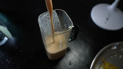 Coffee or chocolate drink being poured into a clear glass jug on a dark kit.. Stock Footage 339022486