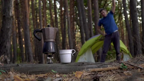 Coffee is prepared in a coffee maker. A man does morning gymnastics near a tent Stock Footage 140859551
