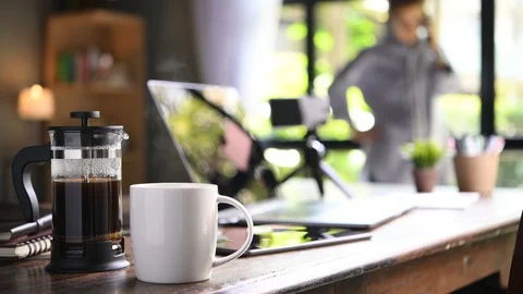 A coffee press and a cup on a work desk with a person working from home Stock Footage 127337021