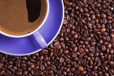 Coffee in purple cup on table surrounded with coffee beans Stock Photos