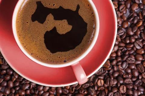 Coffee in red cup on a table surrounded by coffee beans. Stock Photos