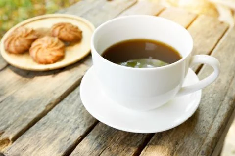 Coffee is served in a white cup, placed on a wooden table with a cookie. It i Stock Photos