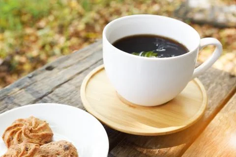 Coffee is served in a white cup, placed on a wooden table with a cookie. It i Stock Photos