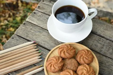 Coffee is served in a white cup, placed on a wooden table with a cookie. It i Stock Photos