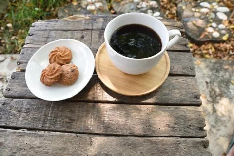 Coffee is served in a white cup, placed on a wooden table with a cookie. It i Stock Photos