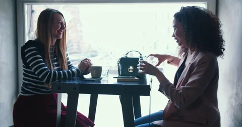 Coffee shop interview. Two happy beautiful multiethnic female friends meeting Stock Footage 144227574