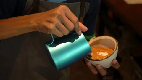 Coffee shop worker in apron pours milk creating cafe latte art in cup. Vídeo Stock 334648408
