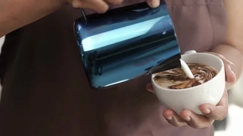 Coffee shop worker in apron pours milk creating cafe latte art in cup. Stock-Footage 334648561