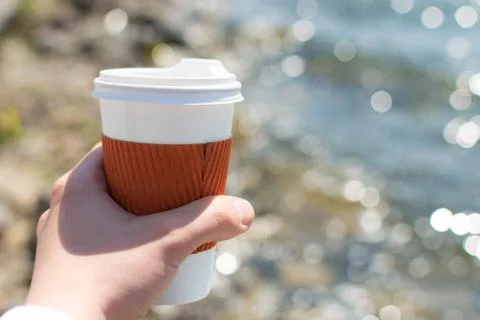 Coffee single cup in hand on the background of the lake in bokeh Foto stock
