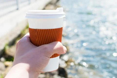Coffee single cup in hand on the background of the lake in bokeh Foto stock