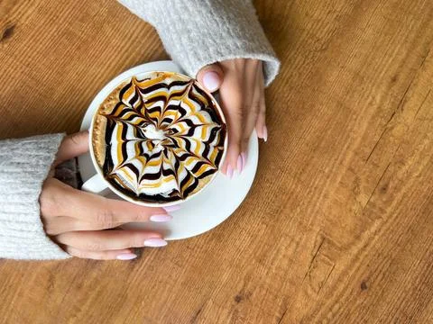 Coffee with spider web pattern on top of foam in white cup and girl's hands on Stock Photos
