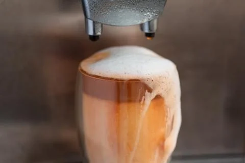 Coffee streaming from coffee machine and pouring out of glass full of milk fo Stock Photos