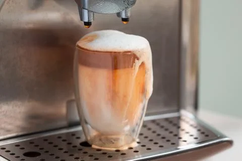 Coffee streaming from coffee machine and pouring out of glass full of milk fo Stock Photos