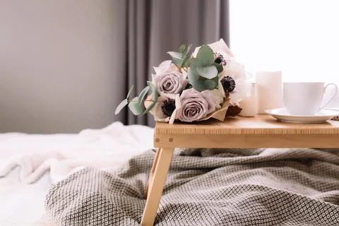Coffee table on bed. Flowers, coffee cup and candles. Interior gray tones, pl Stock Photos