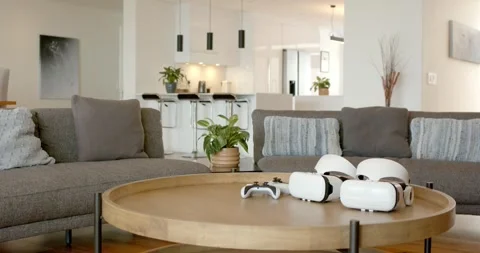 Coffee table is featuring two VR headsets and game controller while sitting in Stock Footage 338435057
