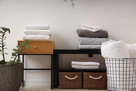 Coffee tables with baskets, bed sheets and houseplant near white wall in livi Stock Photos