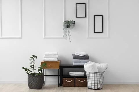 Coffee tables with baskets, bed sheets and houseplants near white wall in liv Stock Photos