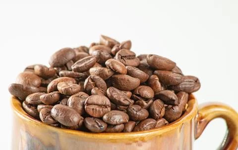 Coffee theme. Ceramic cup filled to the brim with coffee beans on a white Stock Photos