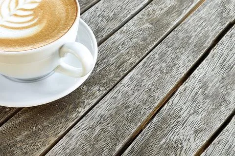 Coffee in white cup with pattern on top of foam, against background of wooden Stock Photos