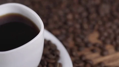 Coffee in white cup surrounded by coffee beans on dark background in 4k UHD Stock Footage 74945907
