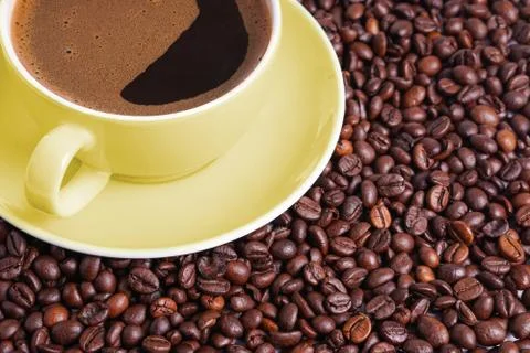 Coffee in yellow cup on a table surrounded by coffee beans. Stock Photos
