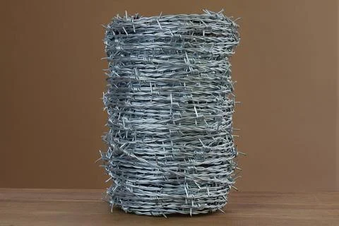 Coiled barbed wire bundle on wooden surface against plain background Stock Photos
