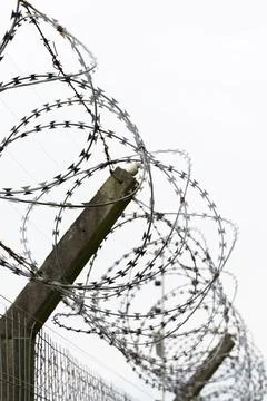 Coiled barbed wire wraps around a weathered fence post Stock Photos
