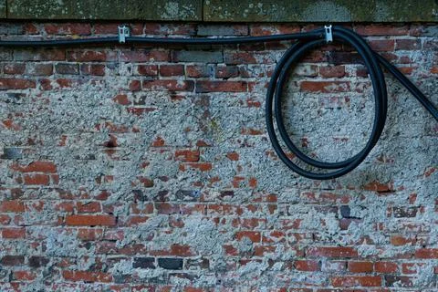 Coiled black cable against weathered brick wall outdoors Stock Photos