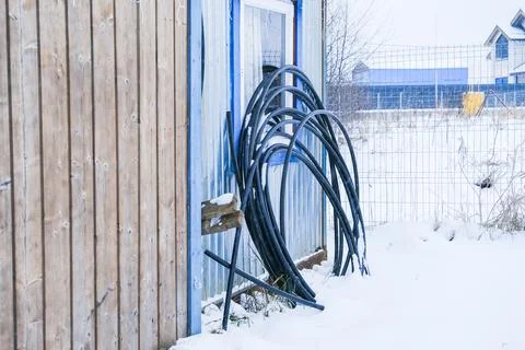 Coiled black cables lean against a blue metallic wall, next to a wooden fence Stock Photos