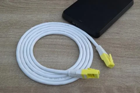 Coiled Ethernet network cable and external hard drive on wooden surface. Stock Photos