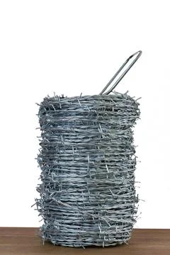 Coiled galvanized barbed wire spool isolated on white background tabletop Stock-Fotos
