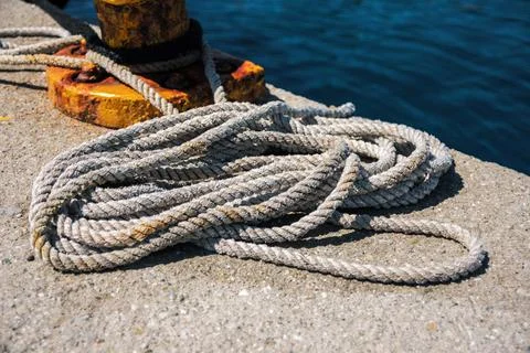 Coiled nautical rope lying on concrete pier next to yellow bollard Stock Photos