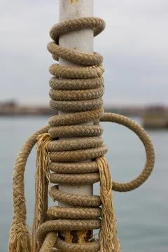 Coiled Nautical Rope Wrapped Around a Weathered Harbor Post Foto stock