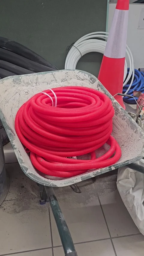 Coiled red pipe hose inside metal wheelbarrow at construction site with safety Stock Footage 348409257