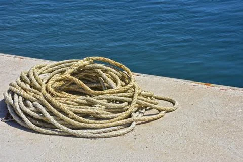Coiled rope on harbor dock with blue sea background, nautical detail Stock Photos